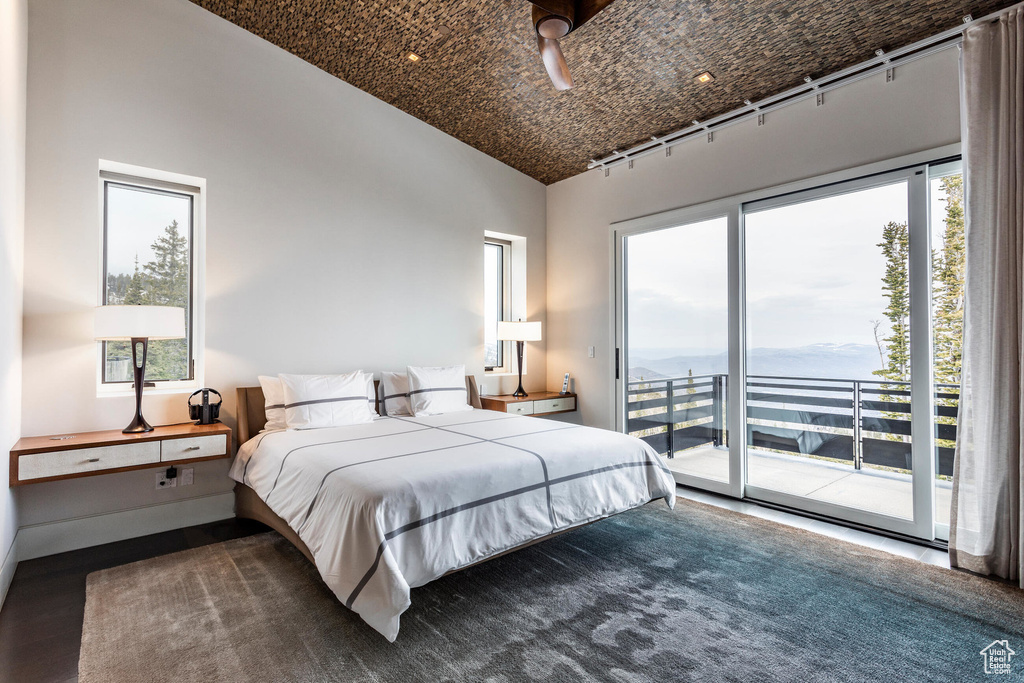 Bedroom with access to outside, vaulted ceiling, multiple windows, and wood finished floors