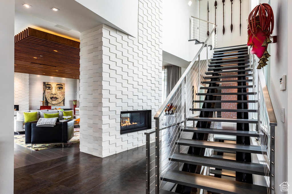Stairs with a towering ceiling, a brick fireplace, and wood finished floors
