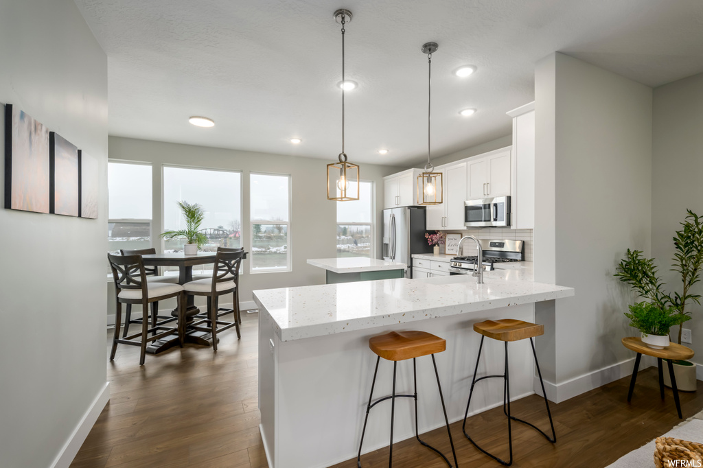 Kitchen featuring dark hardwood / wood-style flooring, appliances with stainless steel finishes, backsplash, decorative light fixtures, and white cabinets