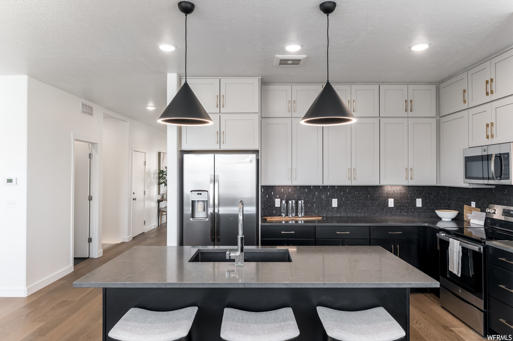 Kitchen with tasteful backsplash, light wood-type flooring, appliances with stainless steel finishes, and pendant lighting
