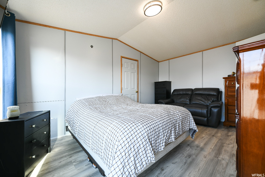 Bedroom with crown molding, vaulted ceiling, a textured ceiling, and hardwood / wood-style floors