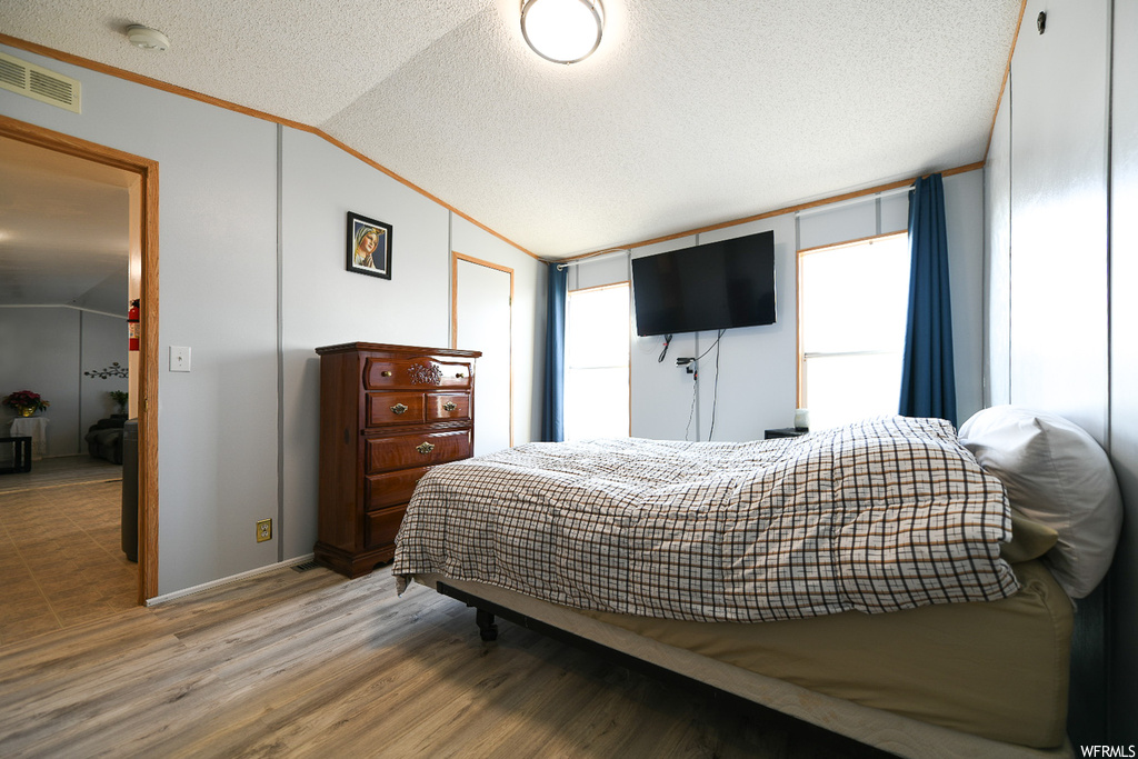 Bedroom featuring lofted ceiling, hardwood / wood-style floors, crown molding, and a textured ceiling