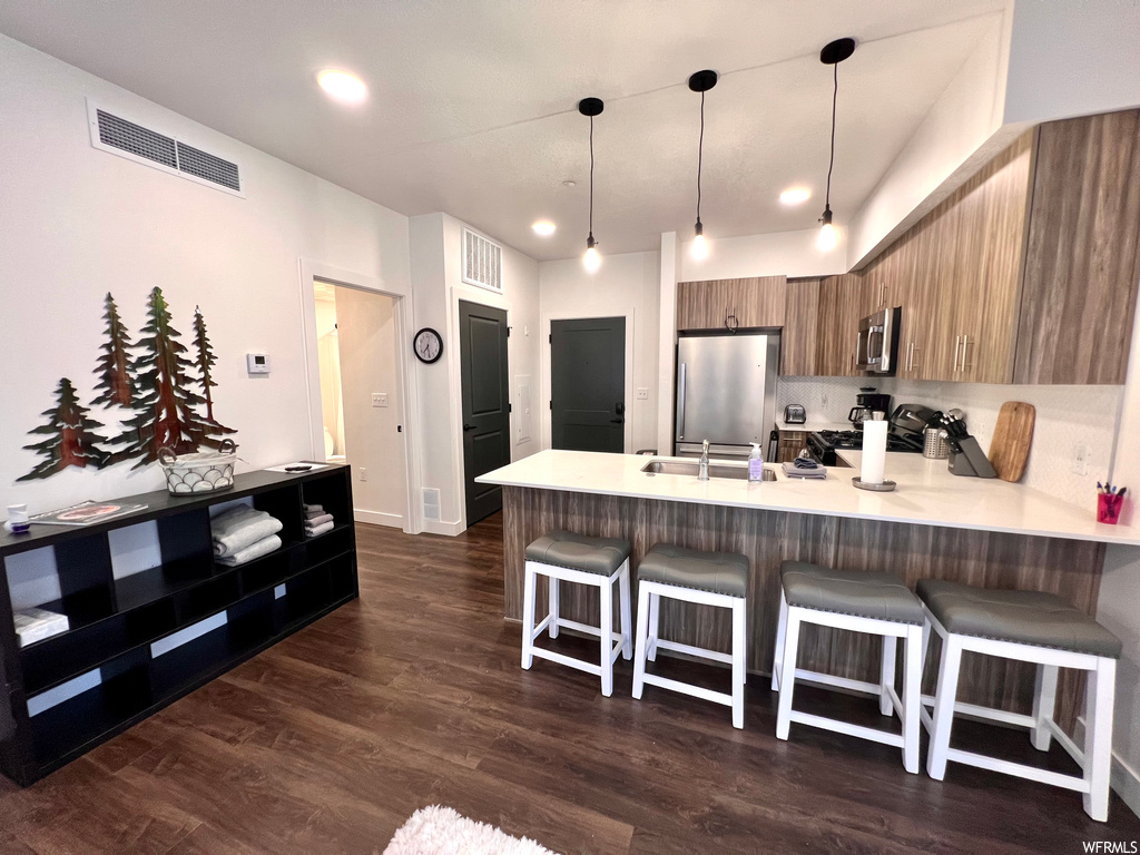 Kitchen featuring dark hardwood / wood-style flooring, kitchen peninsula, a breakfast bar area, hanging light fixtures, and appliances with stainless steel finishes