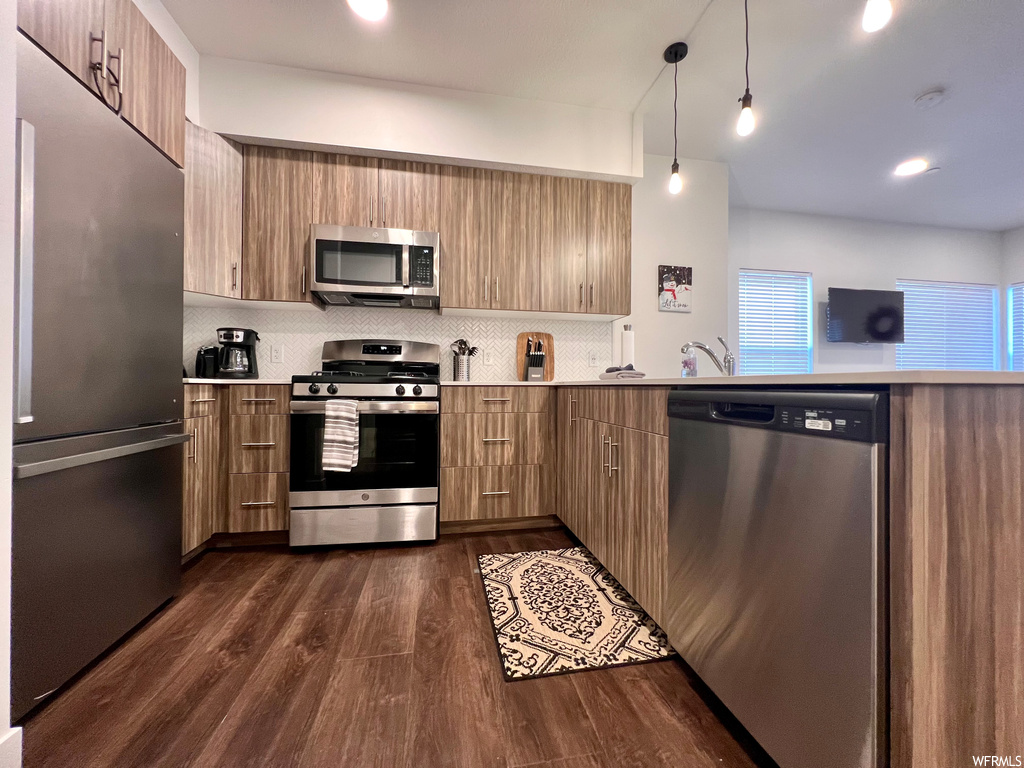Kitchen with decorative light fixtures, stainless steel appliances, sink, tasteful backsplash, and dark hardwood / wood-style floors