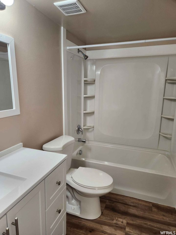 Full bathroom with large vanity, toilet,  shower combination, and hardwood / wood-style flooring