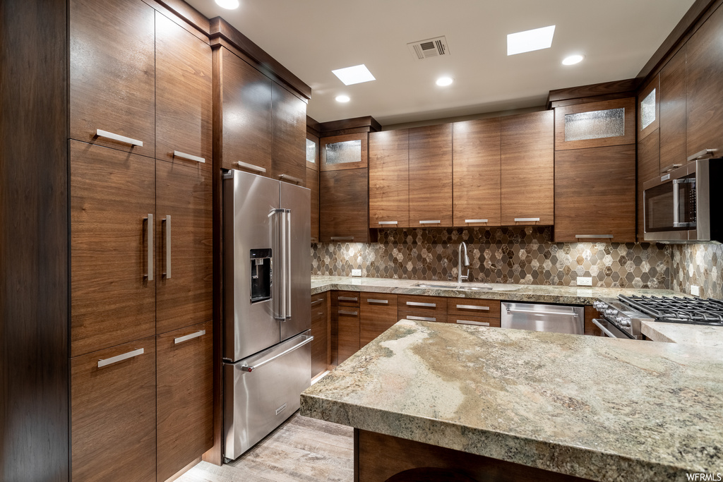 Kitchen with tasteful backsplash, light hardwood / wood-style floors, high quality appliances, and sink