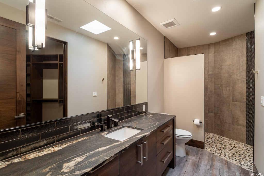 Bathroom with toilet, vanity, hardwood / wood-style floors, backsplash, and a tile shower