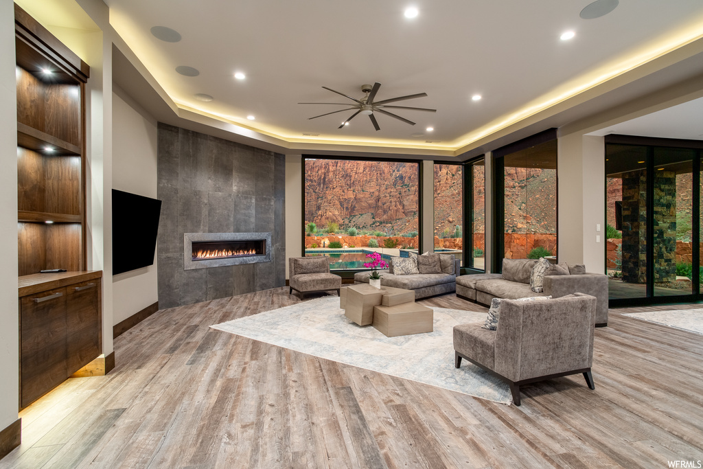 Living room with light hardwood / wood-style flooring, a tile fireplace, ceiling fan, and a raised ceiling