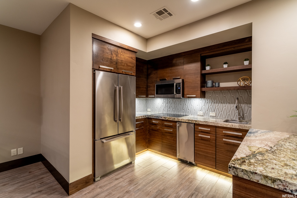 Kitchen featuring appliances with stainless steel finishes, light stone counters, backsplash, sink, and light wood-type flooring