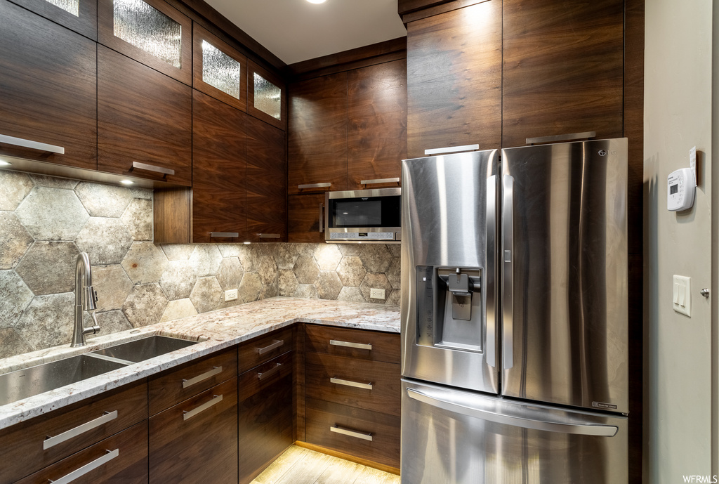 Kitchen with sink, light stone countertops, tasteful backsplash, stainless steel appliances, and light wood-type flooring