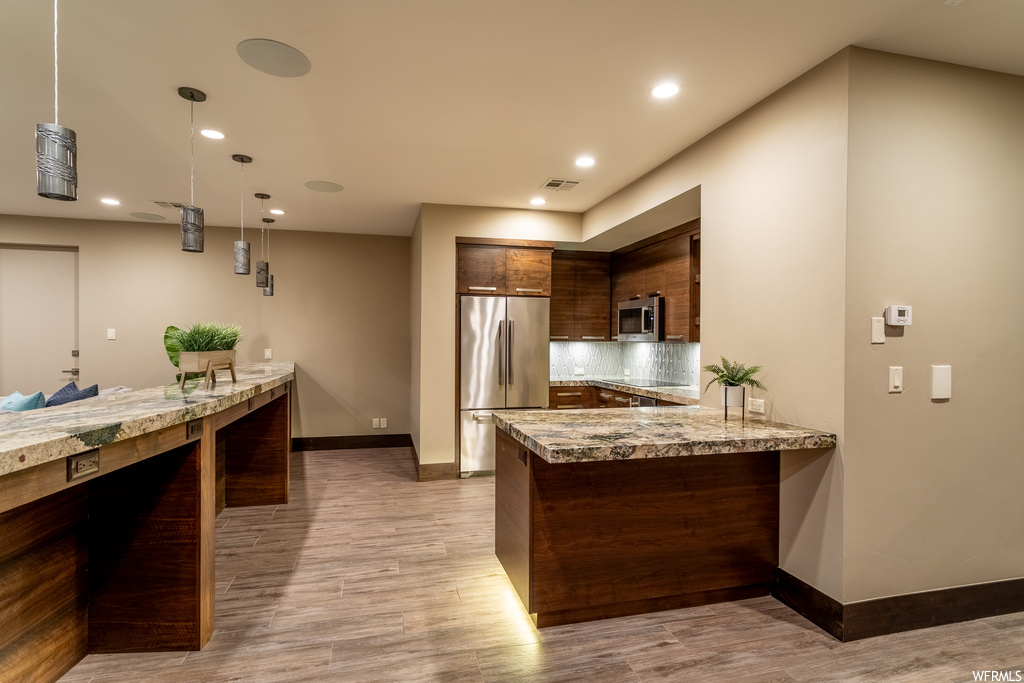 Kitchen with pendant lighting, stainless steel appliances, light stone counters, tasteful backsplash, and dark brown cabinets