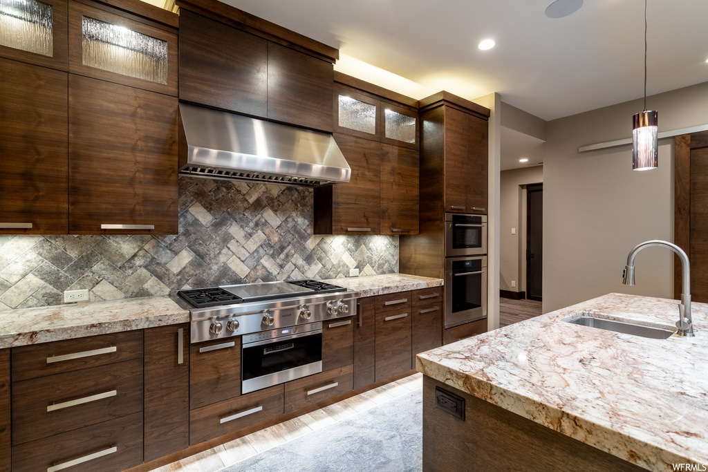 Kitchen featuring sink, wall chimney range hood, appliances with stainless steel finishes, pendant lighting, and backsplash