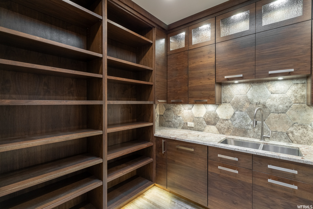 Interior space featuring sink, light wood-type flooring, light stone countertops, and backsplash