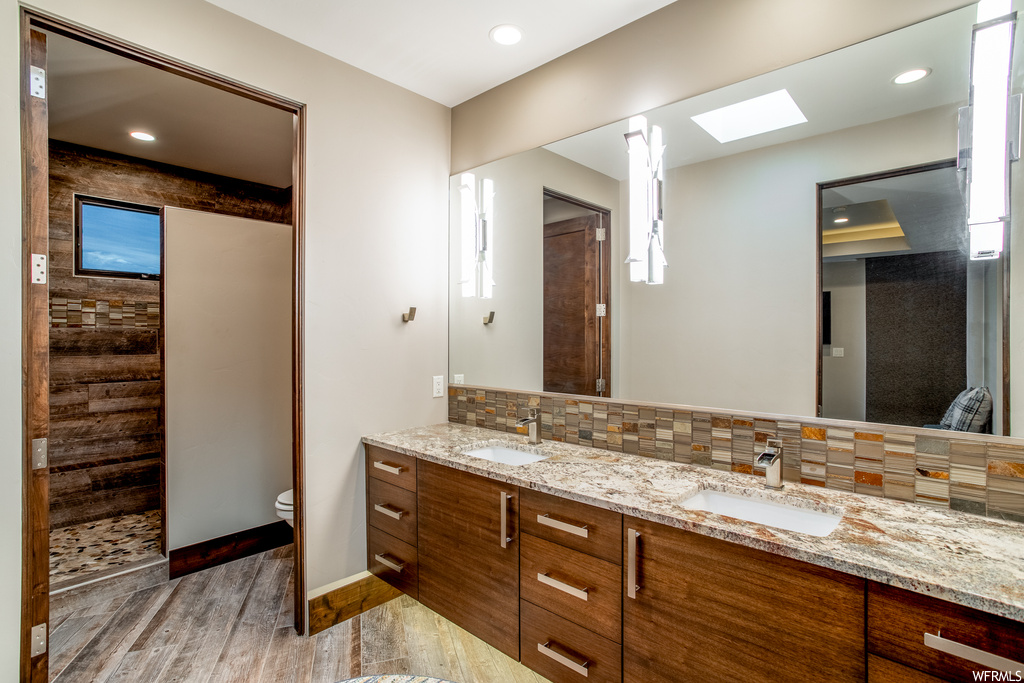 Bathroom with a skylight, double sink, toilet, vanity with extensive cabinet space, and backsplash