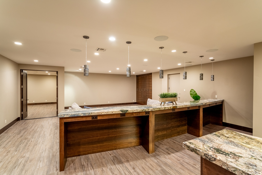 Kitchen with pendant lighting, light hardwood / wood-style floors, a kitchen island, and light stone countertops