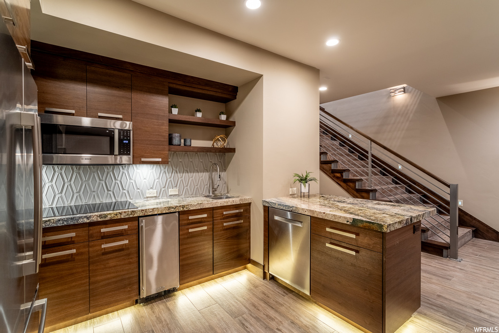 Kitchen with light stone countertops, backsplash, light hardwood / wood-style flooring, sink, and stainless steel appliances