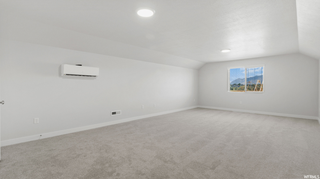 Additional living space featuring vaulted ceiling, light colored carpet, and a wall unit AC