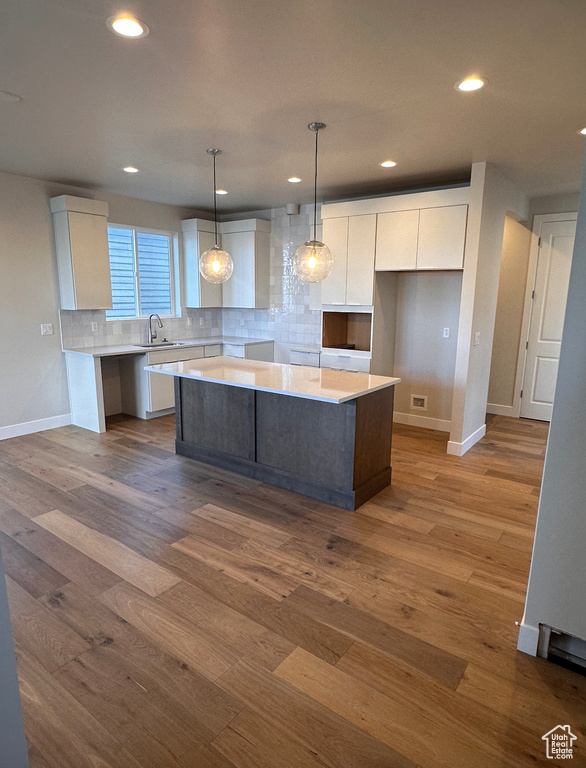 Kitchen with wood-type flooring, hanging light fixtures, a center island, and white cabinetry