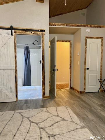 Corridor with a barn door, light hardwood / wood-style flooring, and lofted ceiling
