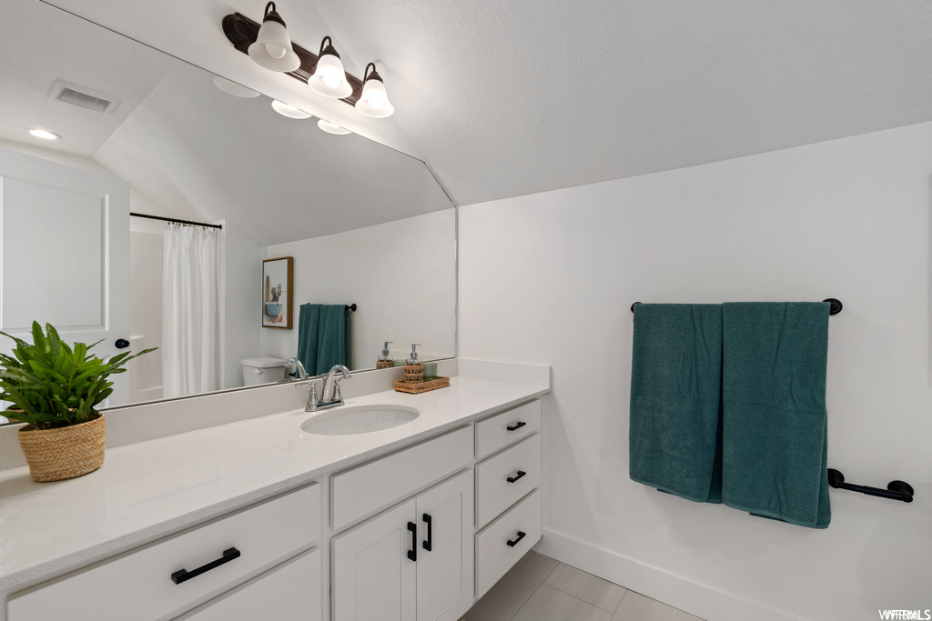 Bathroom featuring lofted ceiling, oversized vanity, toilet, and tile flooring