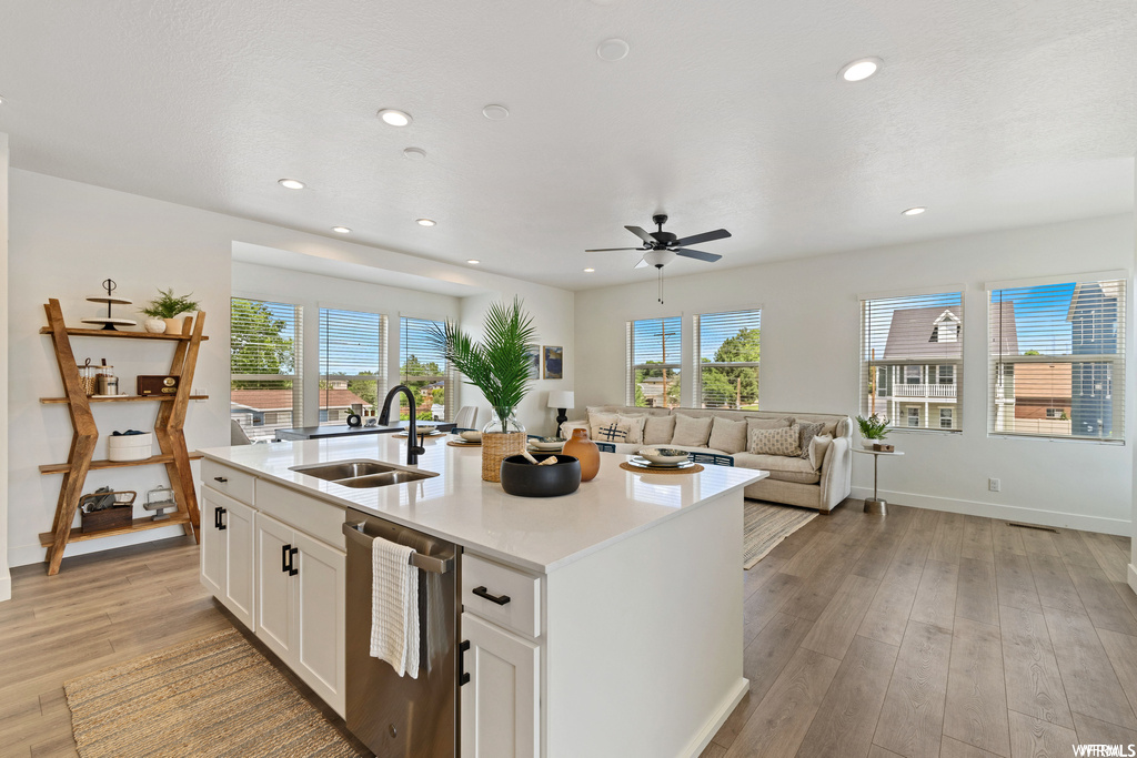 Kitchen with dishwasher, light hardwood / wood-style floors, an island with sink, ceiling fan, and white cabinetry