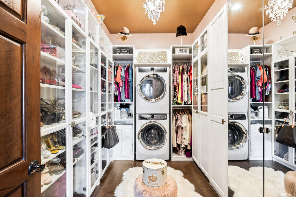 Laundry area featuring a chandelier, stacked washer and clothes dryer, and dark hardwood / wood-style flooring
