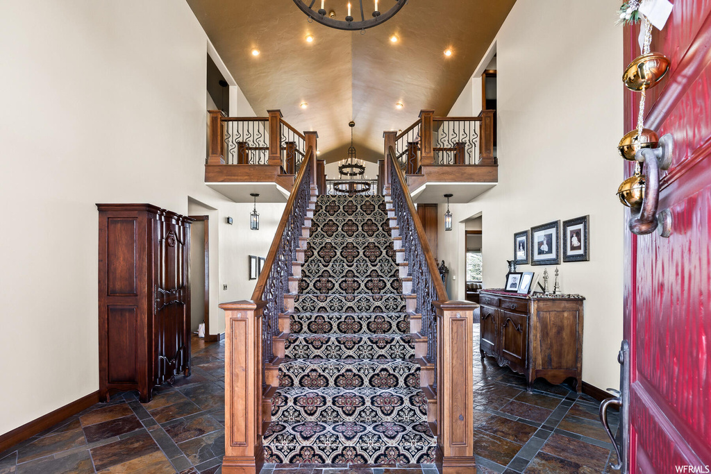 Staircase featuring a notable chandelier, dark tile flooring, and a towering ceiling