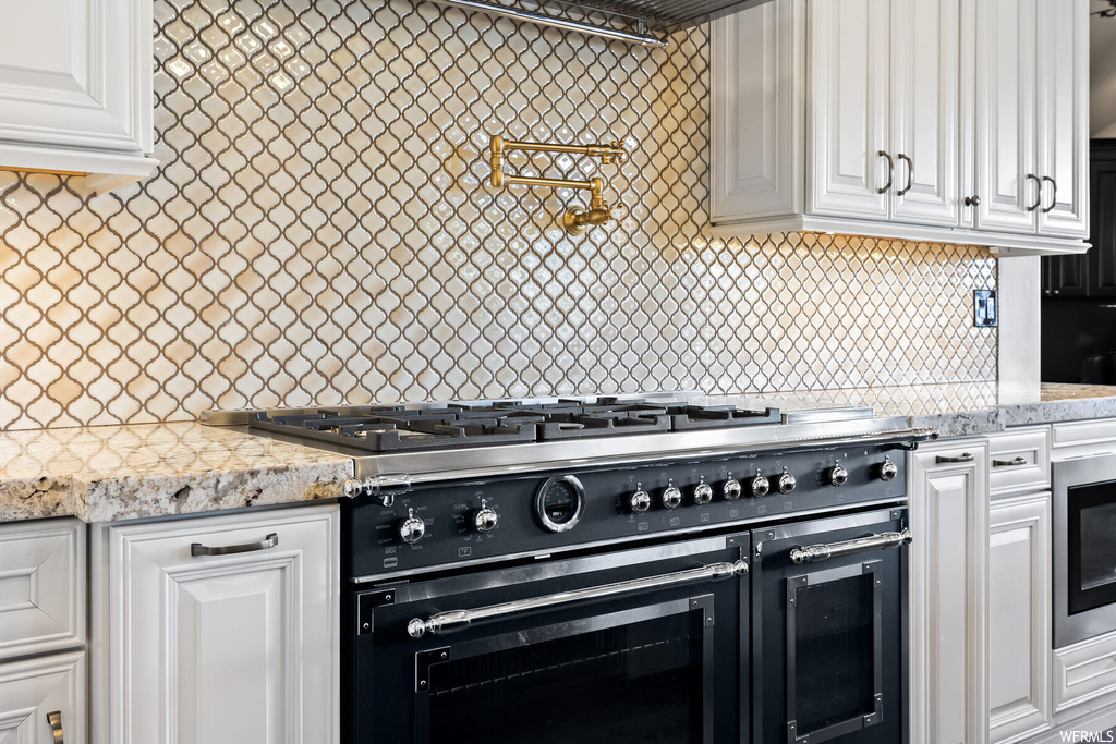 Kitchen featuring tasteful backsplash, white cabinets, light stone countertops, and double oven range