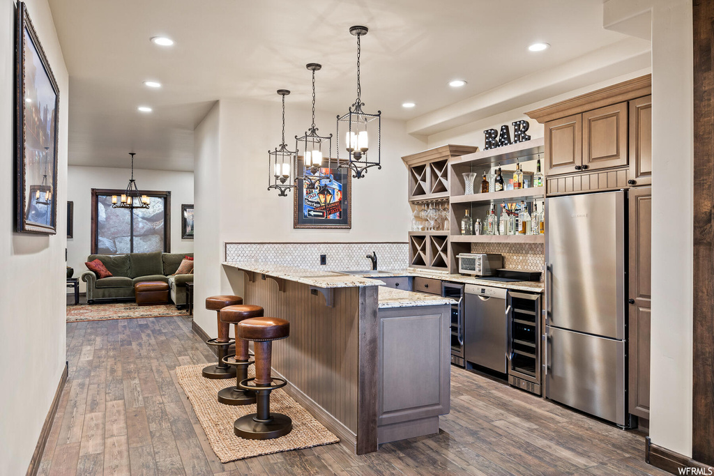 Kitchen with kitchen peninsula, stainless steel refrigerator, wood-type flooring, light stone counters, and tasteful backsplash