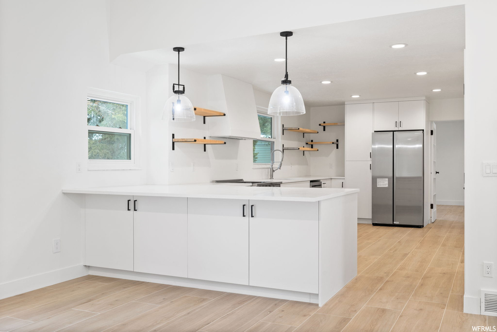 Kitchen with stainless steel fridge, light wood-type flooring, decorative light fixtures, white cabinets, and sink
