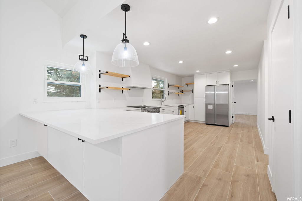 Kitchen with white cabinets, stainless steel fridge, light hardwood / wood-style floors, and hanging light fixtures