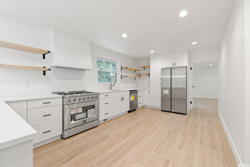 Kitchen featuring sink, white cabinetry, light wood-type flooring, and appliances with stainless steel finishes