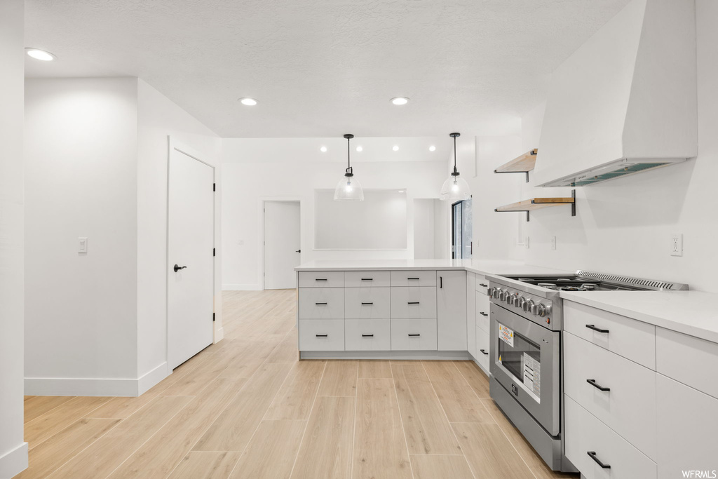 Kitchen with white cabinets, light hardwood / wood-style floors, pendant lighting, custom range hood, and stainless steel stove