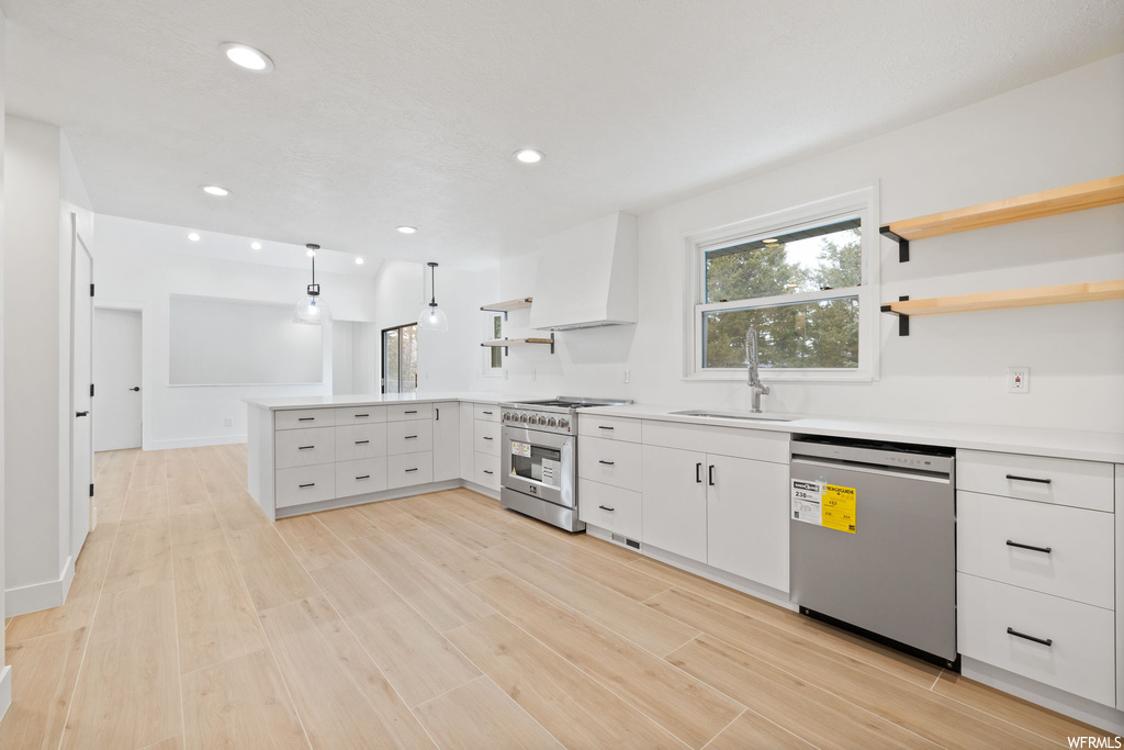 Kitchen featuring white cabinets, appliances with stainless steel finishes, custom range hood, sink, and light wood-type flooring