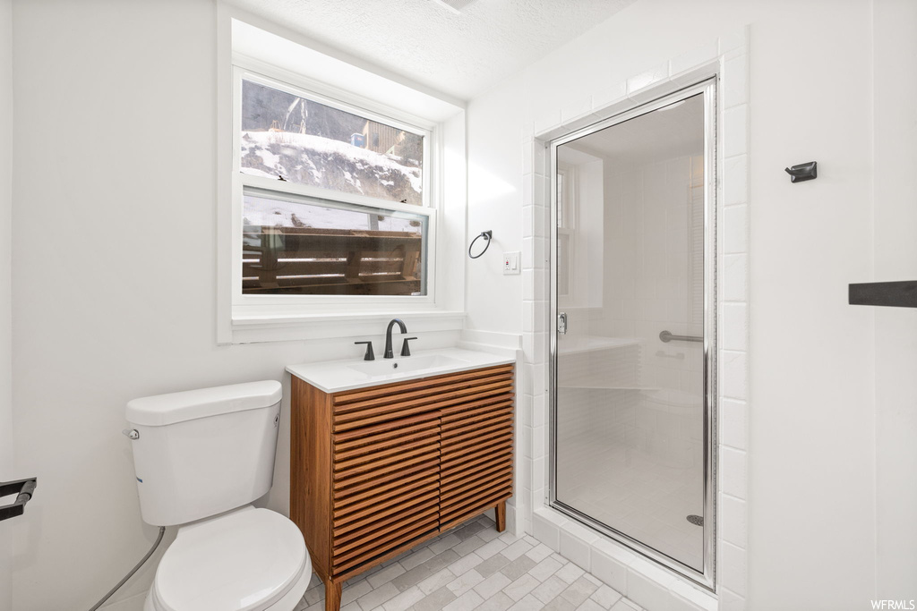 Bathroom featuring toilet, vanity, a shower with shower door, tile flooring, and a textured ceiling