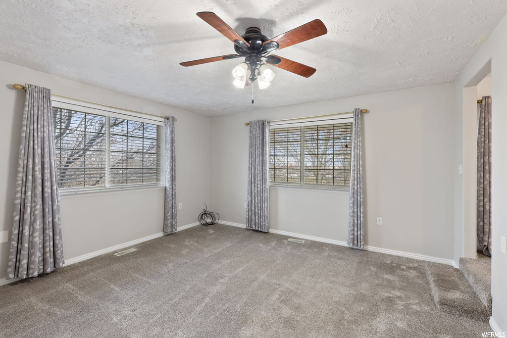 Carpeted spare room with ceiling fan, a textured ceiling, and plenty of natural light