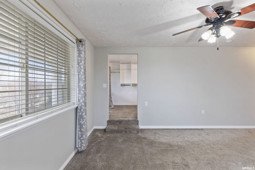 Carpeted empty room featuring plenty of natural light, a textured ceiling, and ceiling fan