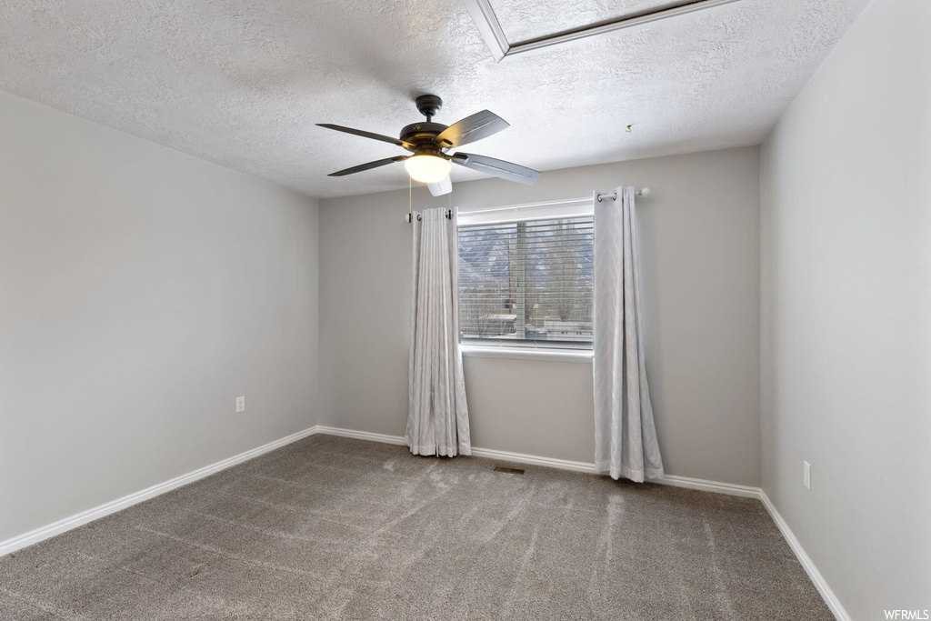 Empty room featuring a skylight, a textured ceiling, dark colored carpet, and ceiling fan