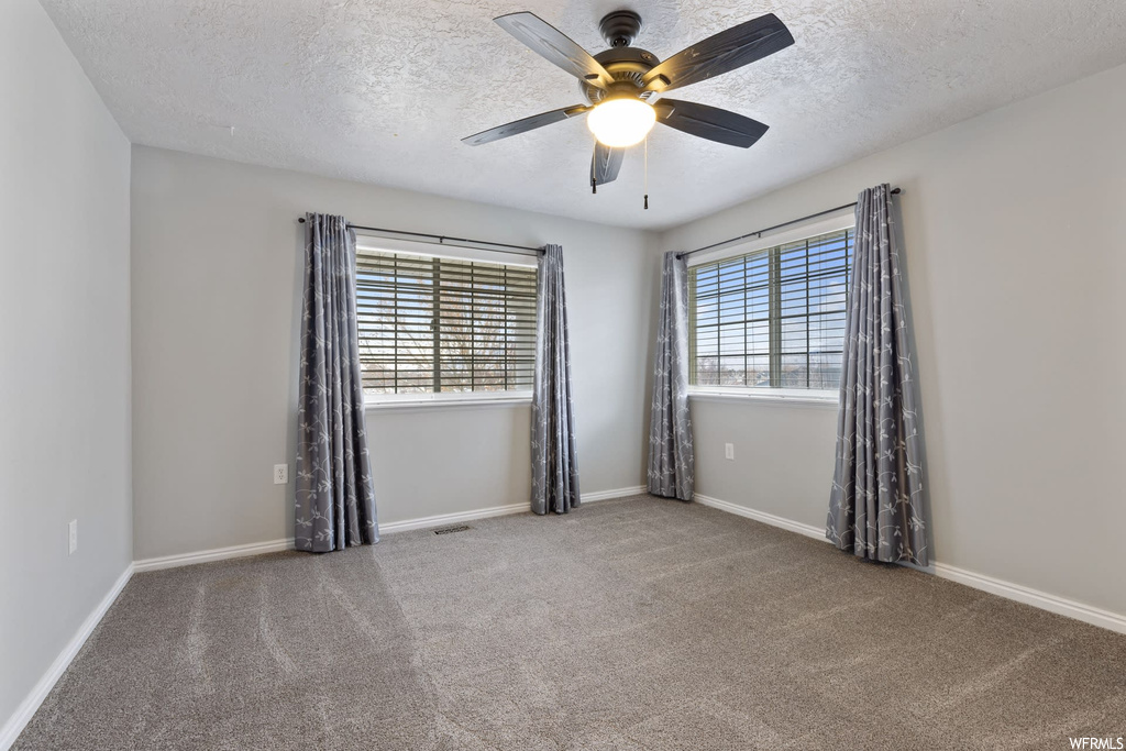 Empty room featuring carpet floors, a textured ceiling, and ceiling fan