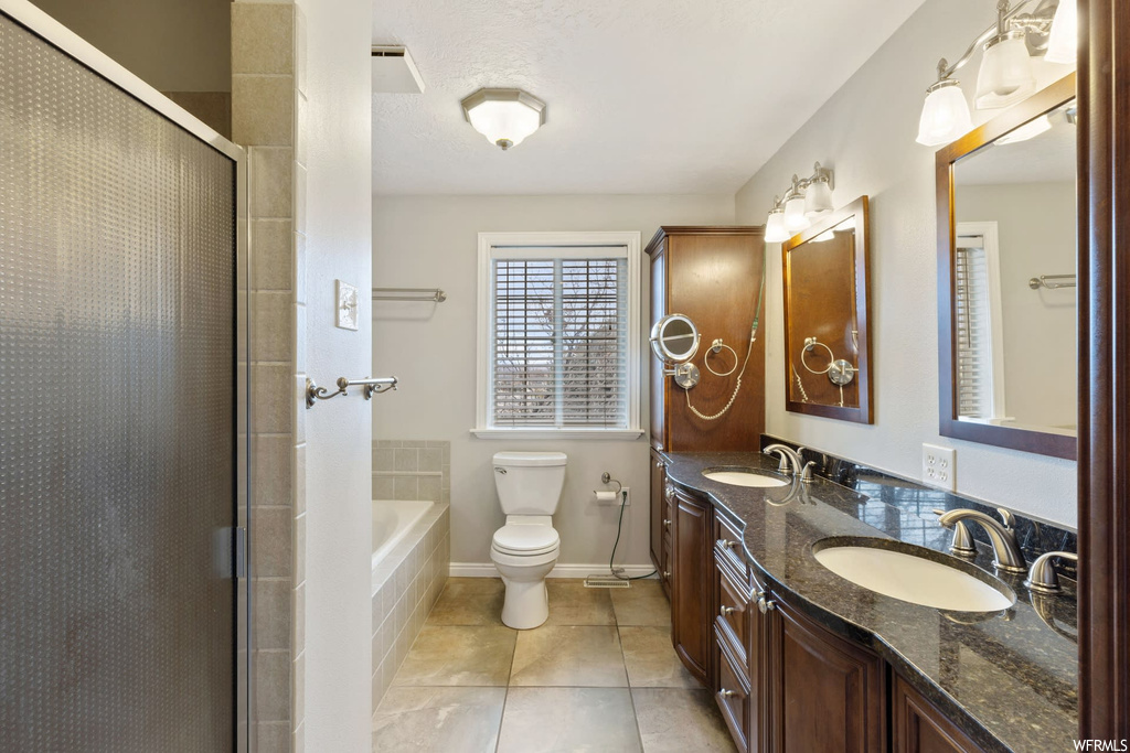 Full bathroom with a textured ceiling, shower with separate bathtub, toilet, double sink vanity, and tile flooring