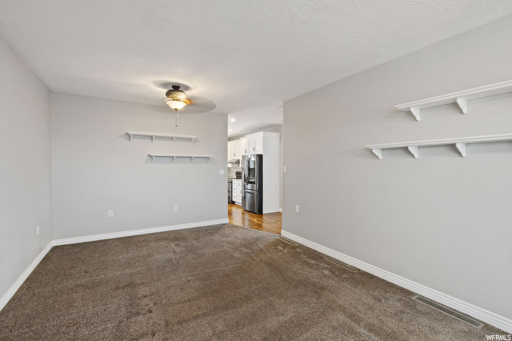 Empty room with a textured ceiling, dark colored carpet, and ceiling fan