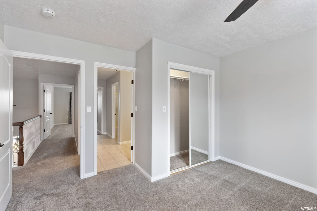 Unfurnished bedroom featuring light colored carpet, a closet, a textured ceiling, and ceiling fan