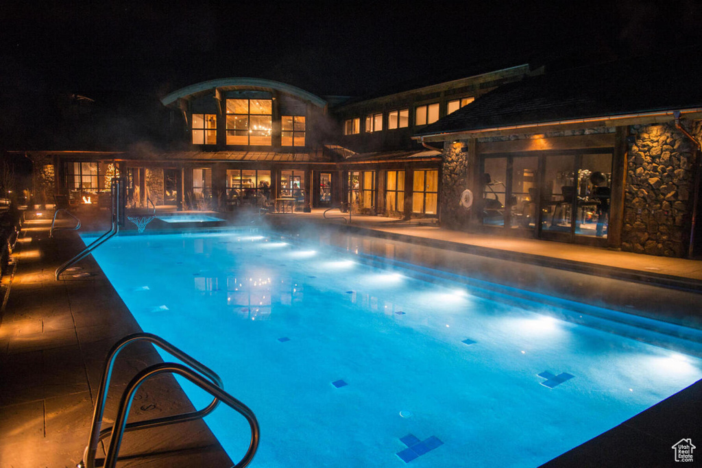 Pool at night with an in ground hot tub and a patio