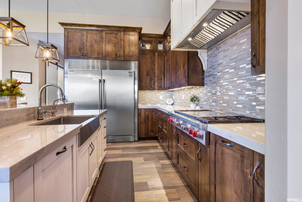 Kitchen featuring custom exhaust hood, decorative light fixtures, light hardwood / wood-style flooring, stainless steel appliances, and tasteful backsplash