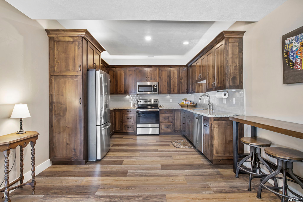 Kitchen featuring light stone countertops, appliances with stainless steel finishes, hardwood / wood-style flooring, backsplash, and sink