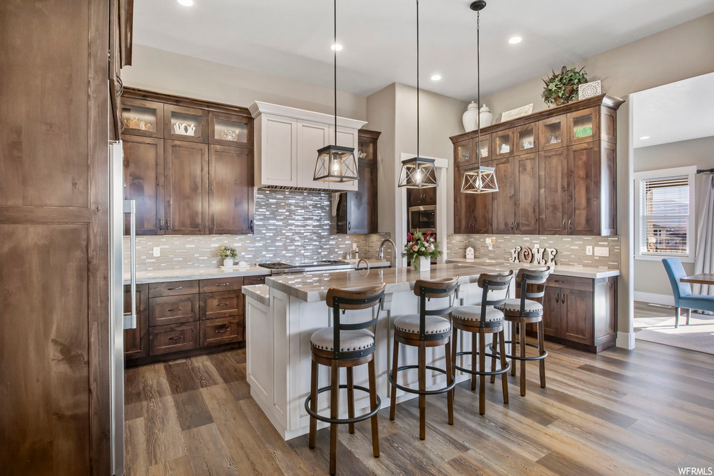 Kitchen featuring hanging light fixtures, tasteful backsplash, dark hardwood / wood-style flooring, and an island with sink