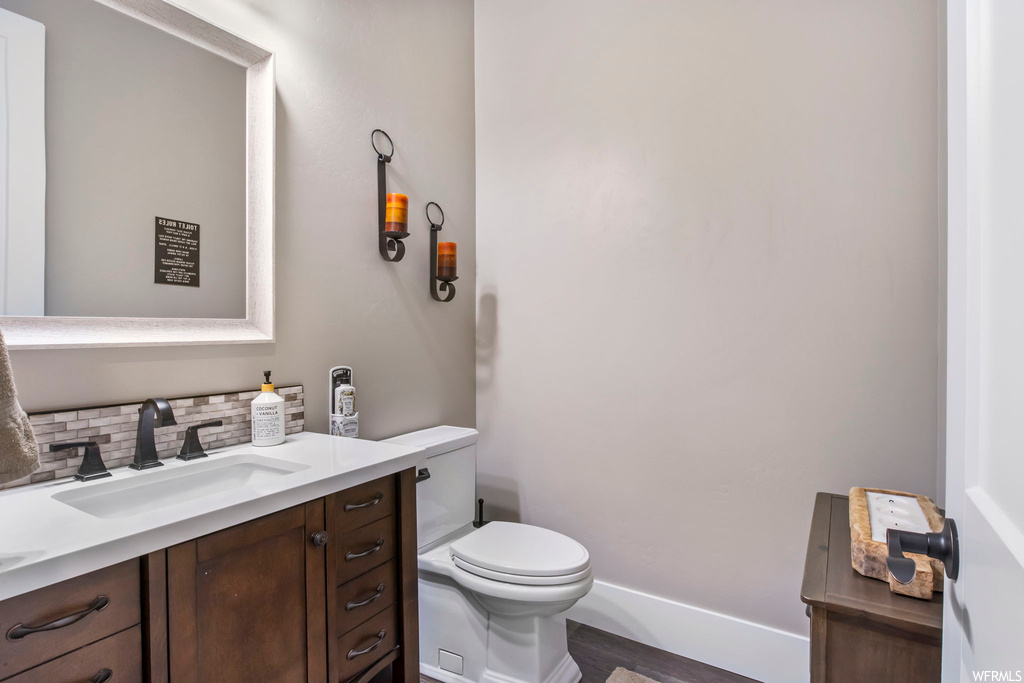 Bathroom featuring hardwood / wood-style flooring, toilet, vanity with extensive cabinet space, and backsplash