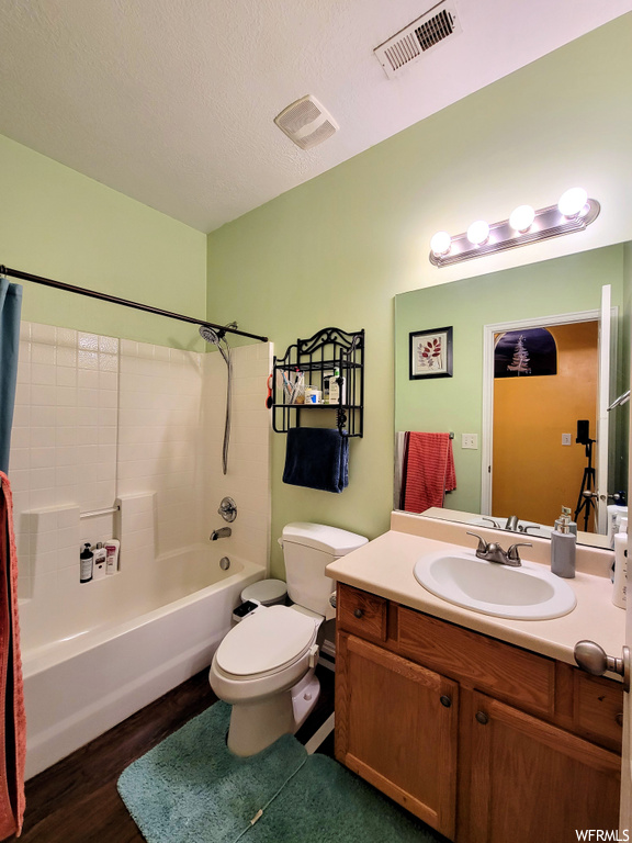 Full bathroom featuring a textured ceiling, oversized vanity, wood-type flooring, toilet, and shower / tub combo with curtain