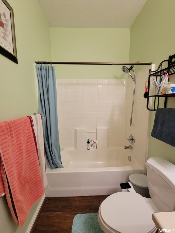 Bathroom featuring toilet, shower / bathtub combination with curtain, and hardwood / wood-style flooring