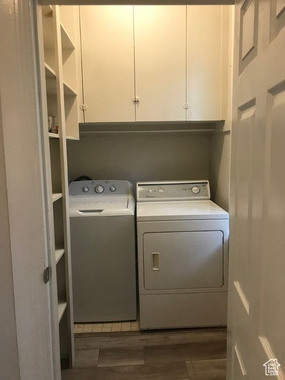 Washroom featuring washer and clothes dryer, cabinets, and dark wood-type flooring